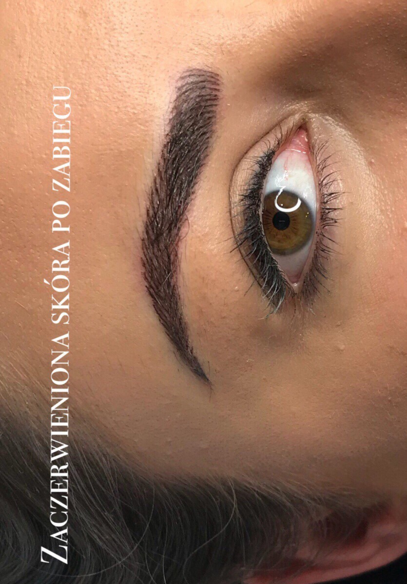 Makro zbliżenie na oko i świeżo wykonany makijaż permanentny brwi; widoczna zaczerwieniona skóra po zabiegu, brązowa tęczówka oka i długie rzęsy.