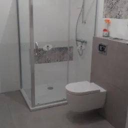 Wyremontowana łazienka z kabiną prysznicową z przesuwanymi drzwiami, podwieszaną toaletą i dekoracyjnymi płytkami na ścianach.