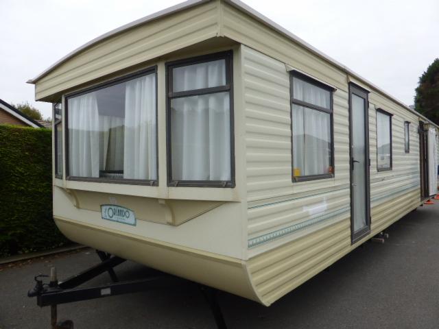 Beżowy domek holenderski z plastikowym sidingiem, widoczne okna z białymi zasłonami, drzwi wejściowe i podwozie z zaczepem.