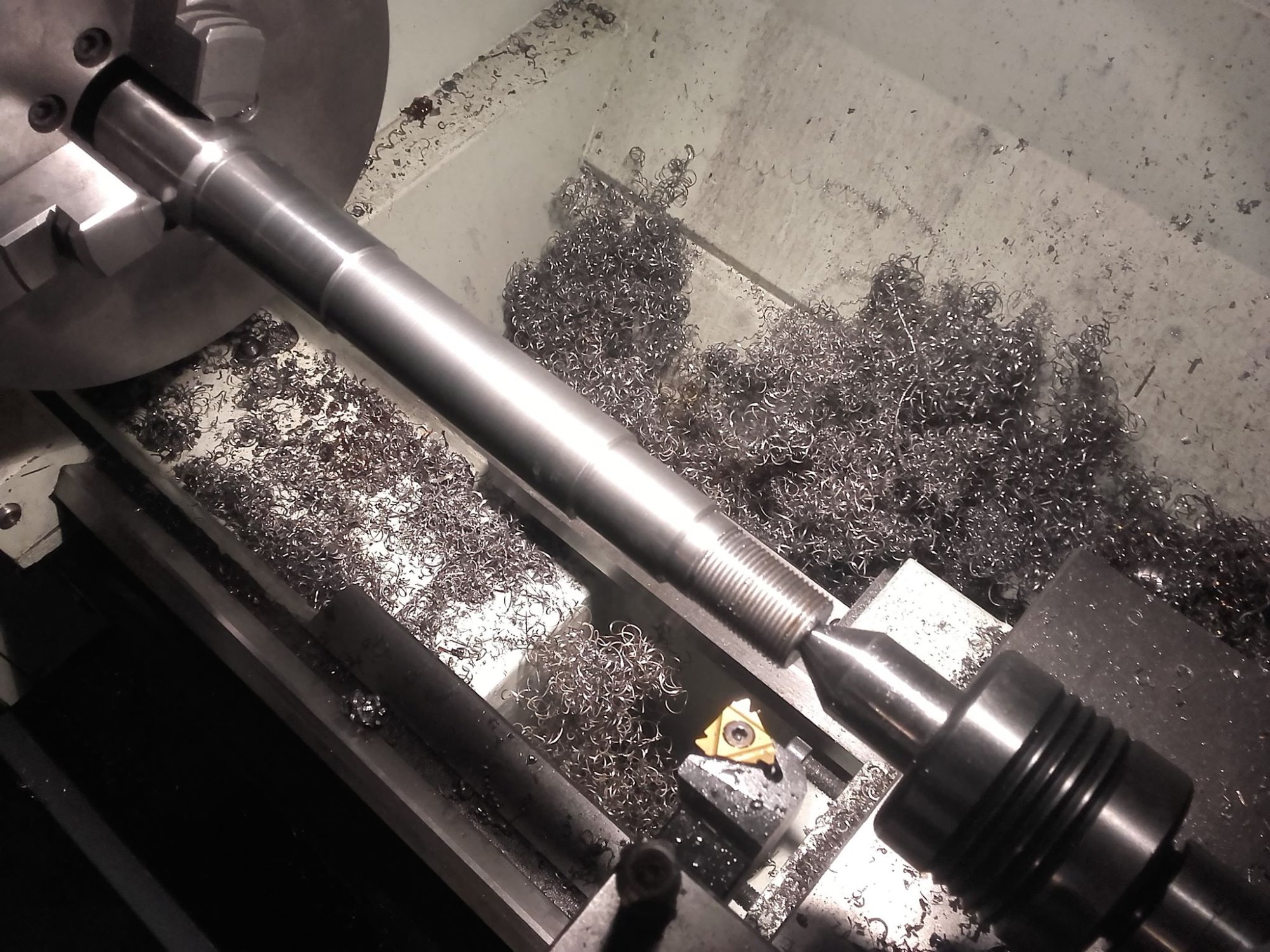 Metalowy wałek obrabiany na tokarce w Jarnołtówku, widoczne wióry i narzędzie skrawające.