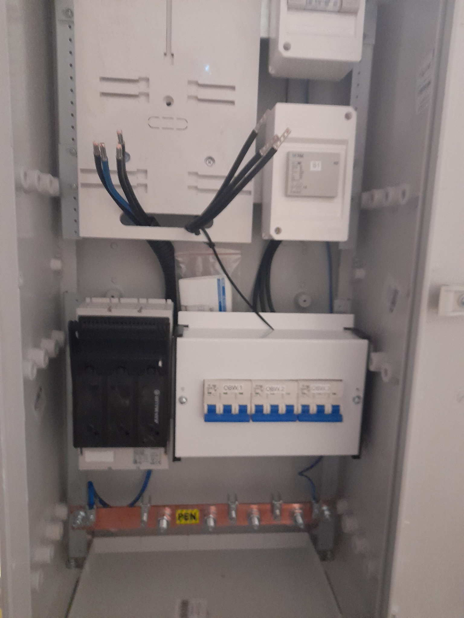 Otwarta skrzynka elektryczna w trakcie montażu, widoczne przewody, bezpieczniki, listwa PEN i elementy mocujące.