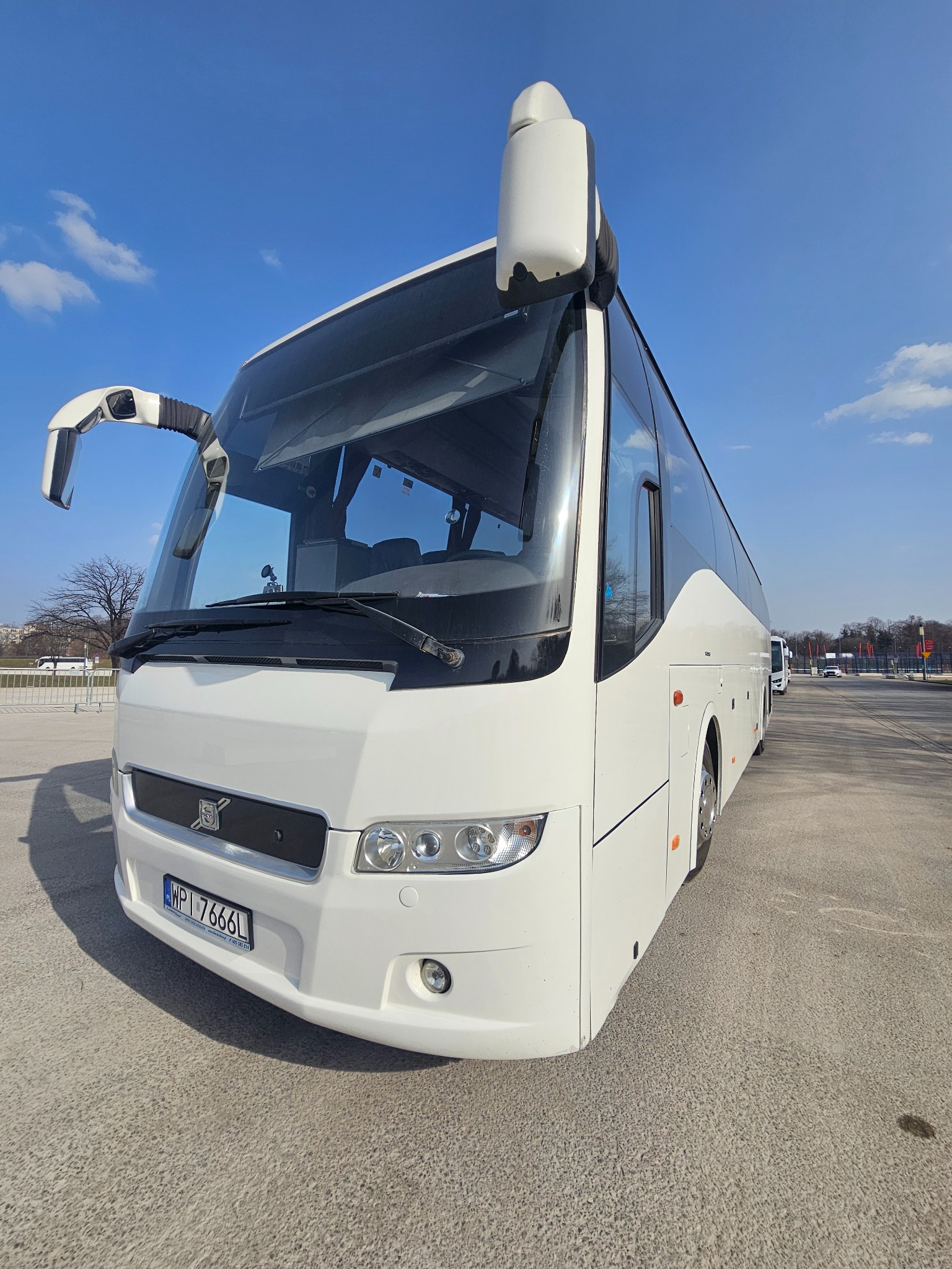 Biały autokar turystyczny Volvo z numerem rejestracyjnym WPI 7666L, zaparkowany na betonowym placu w słoneczny dzień. Widok z boku, lekko od dołu.