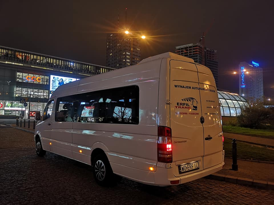 Biały bus marki Sprinter z napisem 'Wynajem autokarów i busów' oraz logo 'Erfil Trans' na tle nocnego krajobrazu Warszawy z budynkiem Novotel i budową drapacza chmur.