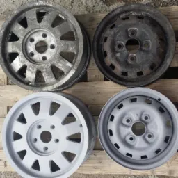 Cztery felgi samochodowe na drewnianej palecie: dwie przed piaskowaniem i malowaniem, z widoczną rdzą i zabrudzeniami, oraz dwie po malowaniu proszkowym na jasnoszaro.