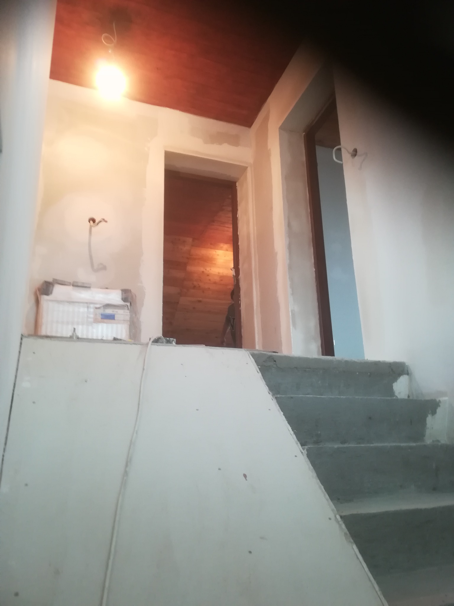 Wnętrze w trakcie prac przygotowawczych: surowe schody prowadzą w górę, ściany częściowo otynkowane, widoczne instalacje elektryczne i fragment drewnianego sufitu w tle.