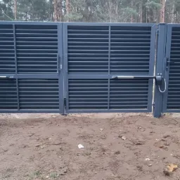 Szara, nowoczesna brama wjazdowa lamelowa z automatyką, częściowo otwarta, na tle leśnym.