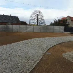 Nawadniany teren przygotowany pod trawnik z rolki, widoczny fragment ścieżki z kostki granitowej i rolka trawy w tle.