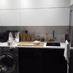 Remix - Nowoczesna kuchnia z białymi szafkami wiszącymi i czarnymi szafkami dolnymi, pralka w zabudowie pod blatem, akcesoria kuchenne na blacie, minimalistyczny styl.