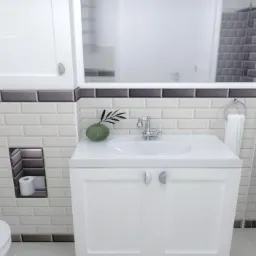 Nowoczesna łazienka z białymi i szarymi płytkami typu metro, białą szafką pod umywalką z okrągłymi uchwytami, lustrem w białej ramie i wnęką na papier toaletowy.