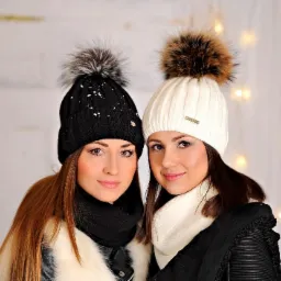 Dwie modelki prezentują zimowe stylizacje: czarna i biała czapka z pomponami, dopasowane szaliki, oświetlenie dekoracyjne w tle.