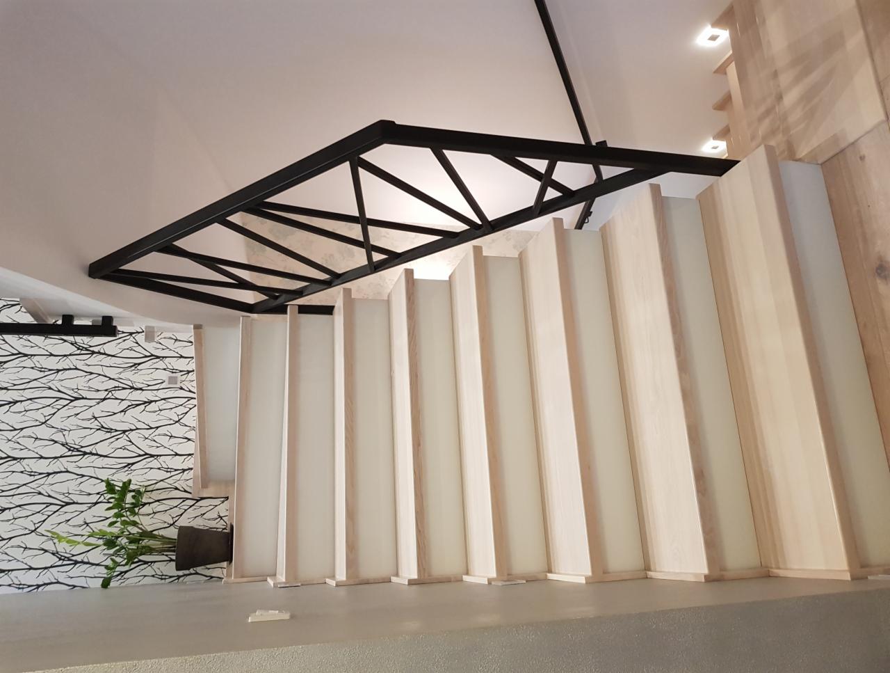 Nowoczesne schody z drewnianymi pionowymi panelami i czarną metalową konstrukcją nad nimi, dekoracyjna tapeta w tle z motywem gałęzi.