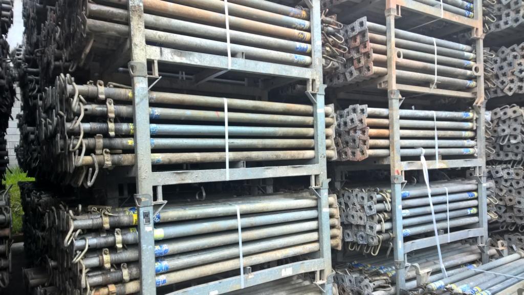 Stalowe podpory budowlane składowane w metalowych regałach, zabezpieczone taśmami, widoczne ślady użytkowania.