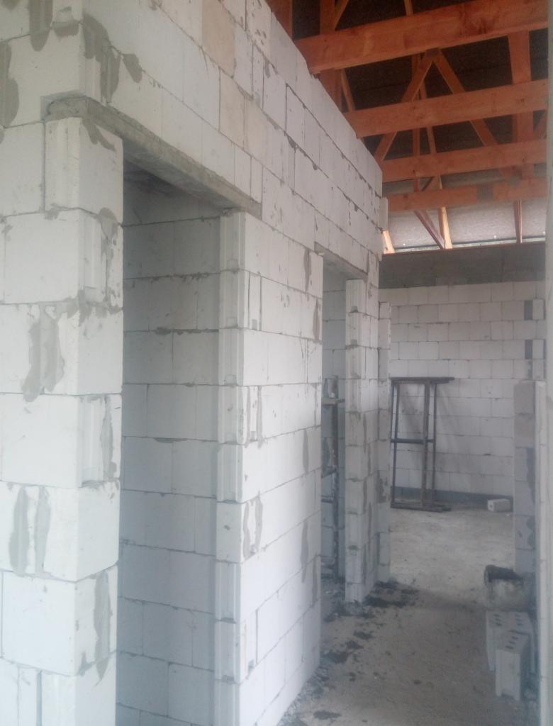Wnętrze w trakcie budowy: ściany z białych bloczków, widoczne nadproża i drewniana konstrukcja dachu, surowy stan.