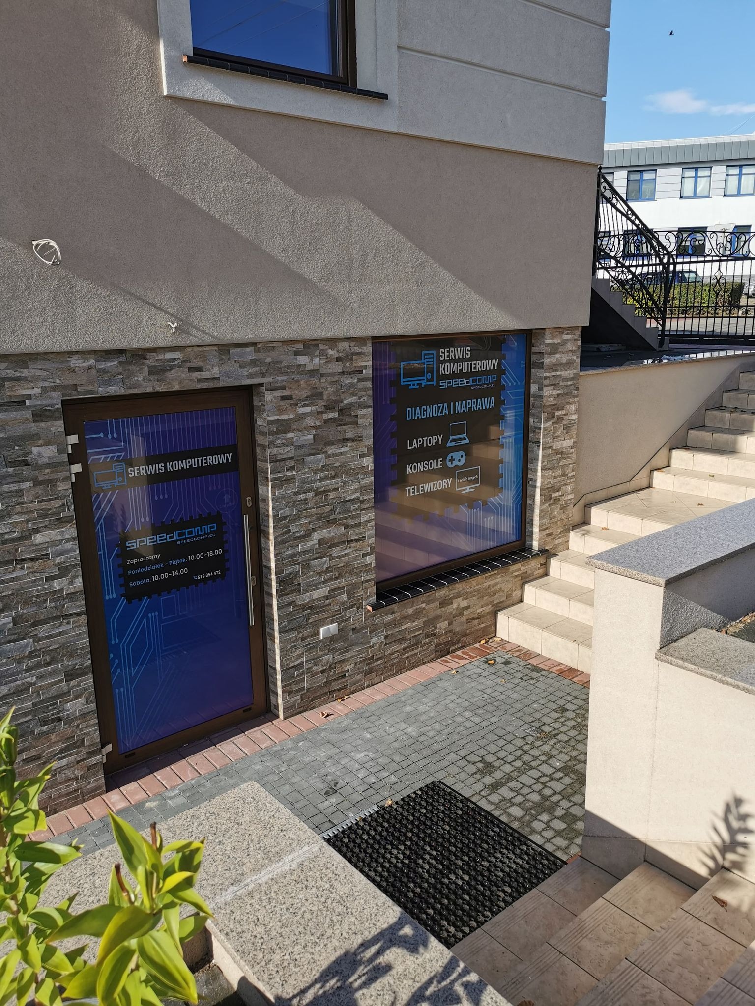 Fasada budynku z wejściem i oknem serwisu komputerowego Speedcomp, z informacją o diagnostyce i naprawie laptopów, konsol i telewizorów.