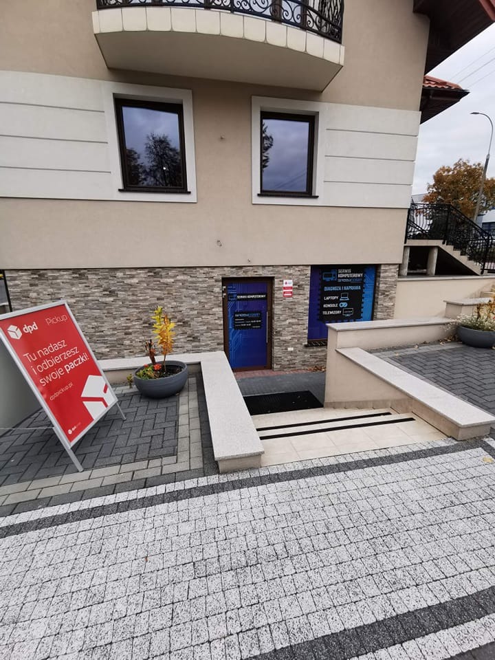Fasada budynku z szyldem serwisu komputerowego widoczna nad wejściem, obok reklama DPD Pickup.