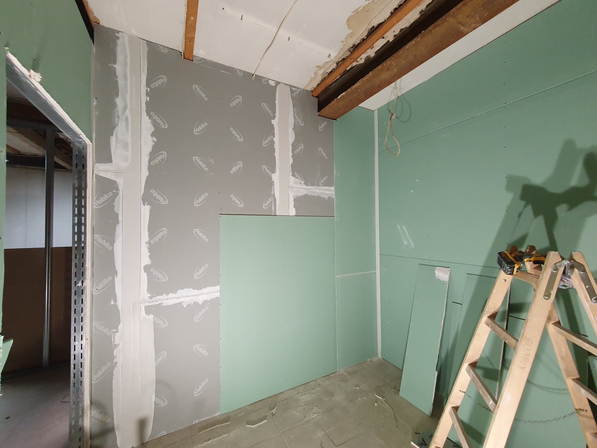 Wnętrze w trakcie montażu ścian działowych z płyt gipsowo-kartonowych Habito, widoczna drabina z wkrętarką, częściowo wyszpachlowane łączenia płyt, surowy strop z drewnianymi belkami.