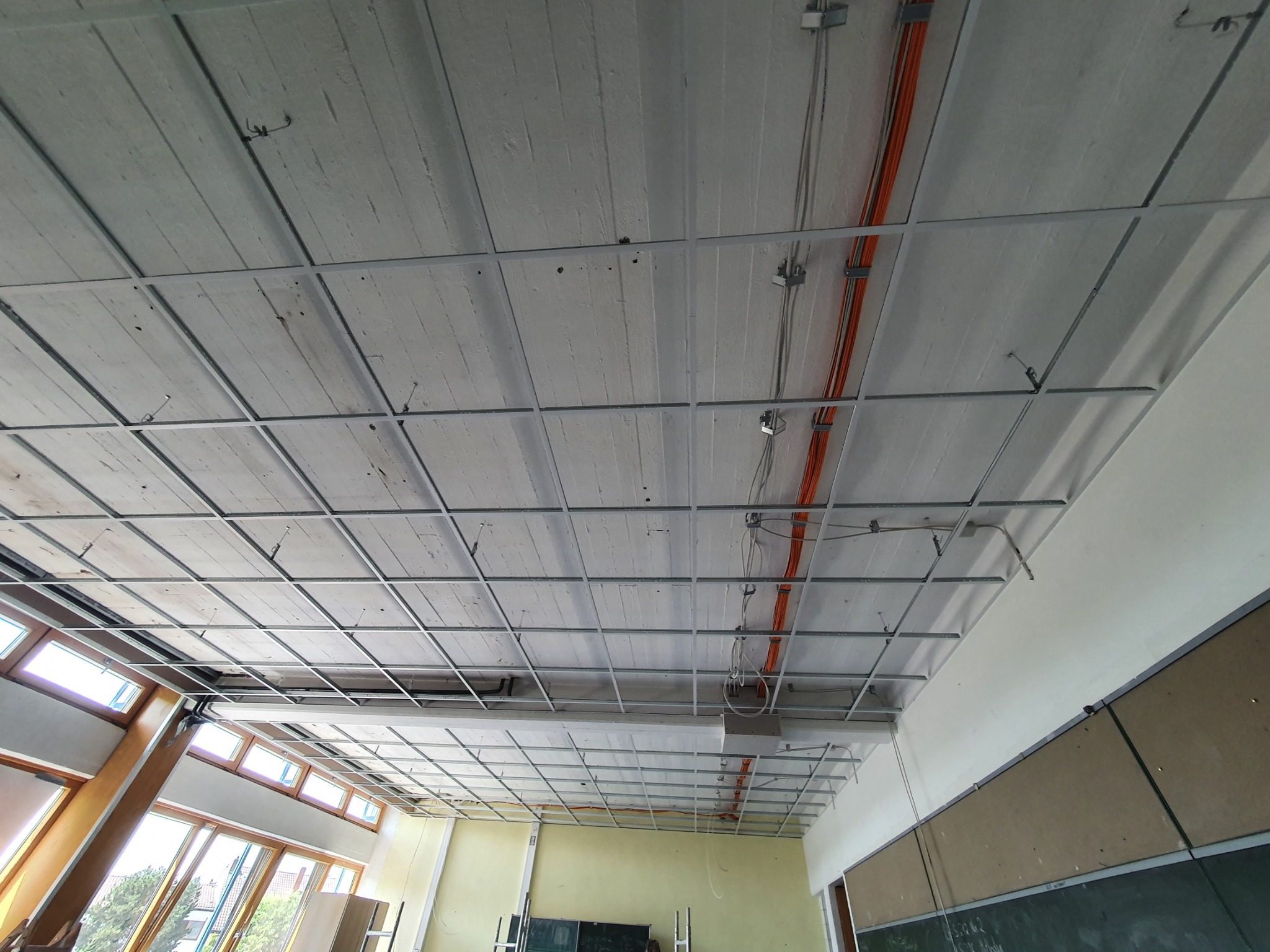 Widok sufitu w trakcie montażu metalowej konstrukcji podwieszanej w Pasłęku, widoczne przewody elektryczne i fragmenty ścian.