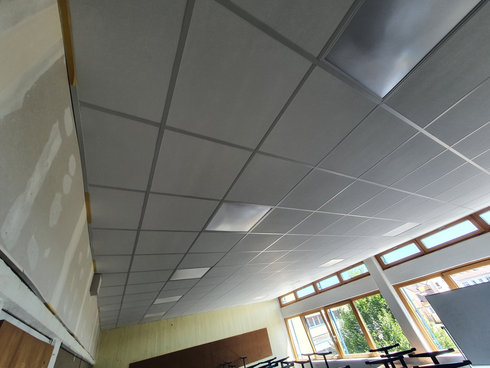 Sufit podwieszany z płyt kartonowo-gipsowych w pomieszczeniu biurowym, widoczne okna i fragment ściany z surowym wykończeniem.
