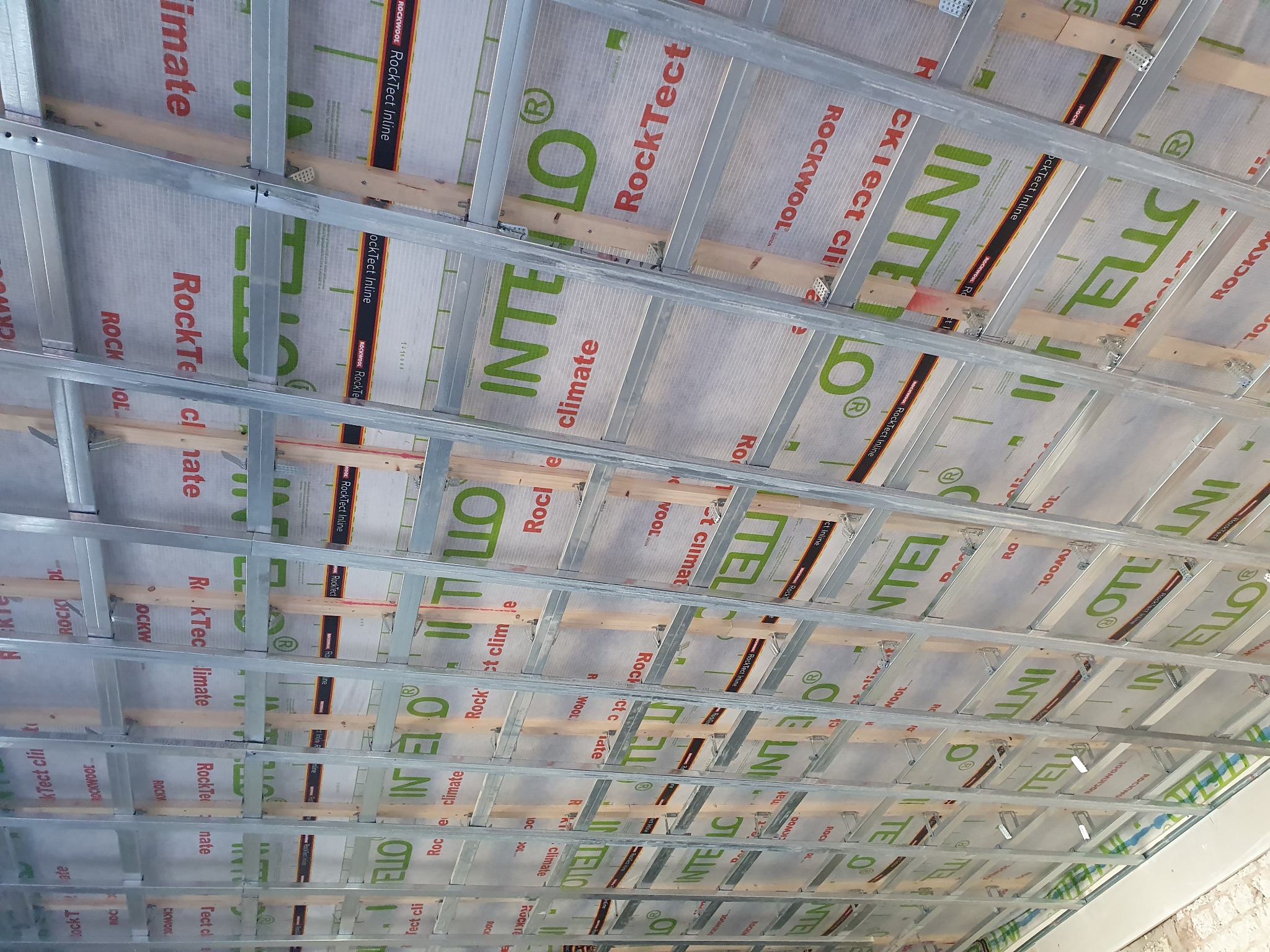 Montaż izolacji termicznej Rockwool z widoczną konstrukcją metalową i drewnianą, tworzącą szkielet pod przyszłą zabudowę, widok z dołu.