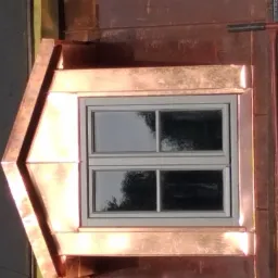 Lukarna z oknem, obłożona miedzianą blachą, widoczne elementy rusztowania.