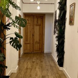 KRSH Sterling & Honest - Kancelaria Prawno - Rachunkowa - Korytarz biurowy z drewnianą podłogą, roślinami i nowoczesnym oświetleniem. W tle dwuskrzydłowe drzwi i pionowa ściana z roślin. Jasne, naturalne światło.