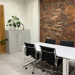 KRSH Sterling & Honest - Kancelaria Prawno - Rachunkowa - Nowoczesne biuro z białym stołem, czarnymi krzesłami i ścianą z czerwonej cegły. Na szafce roślina doniczkowa. Jasne płytki podłogowe. Minimalistyczny design.