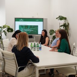 KRSH Sterling & Honest - Kancelaria Prawno - Rachunkowa - Zespół w biurze: pięć kobiet siedzi przy białym stole w sali konferencyjnej, na ścianie monitor z logo firmy. Jasne wnętrze z roślinami doniczkowymi.