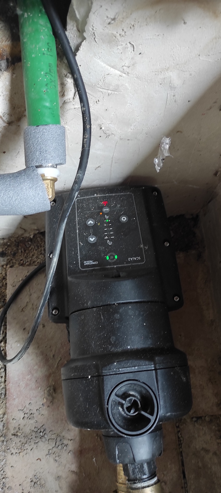 Czarna pompa hydroforowa Scala2 zainstalowana w Stargardzie, widoczne rury z izolacją termiczną i przewody elektryczne, tło stanowi surowa ściana.