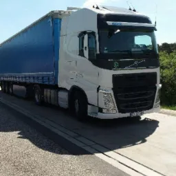 Biała ciężarówka Volvo z niebieską naczepą na betonowej platformie w słoneczny dzień, widoczne tablice rejestracyjne.