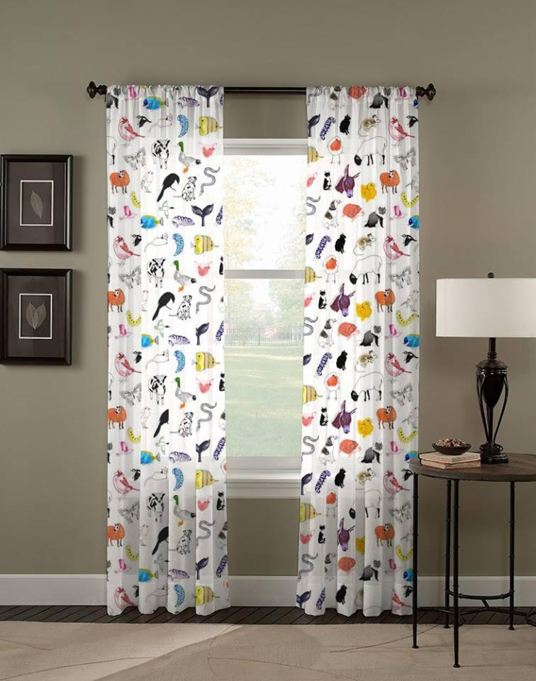 Dwie białe zasłony z nadrukiem zwierząt w różnych kolorach, wiszące w oknie, z lampą na stoliku obok.