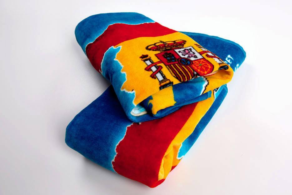 Złożony, miękki ręcznik plażowy z nadrukiem flagi i herbu Hiszpanii na białym tle.