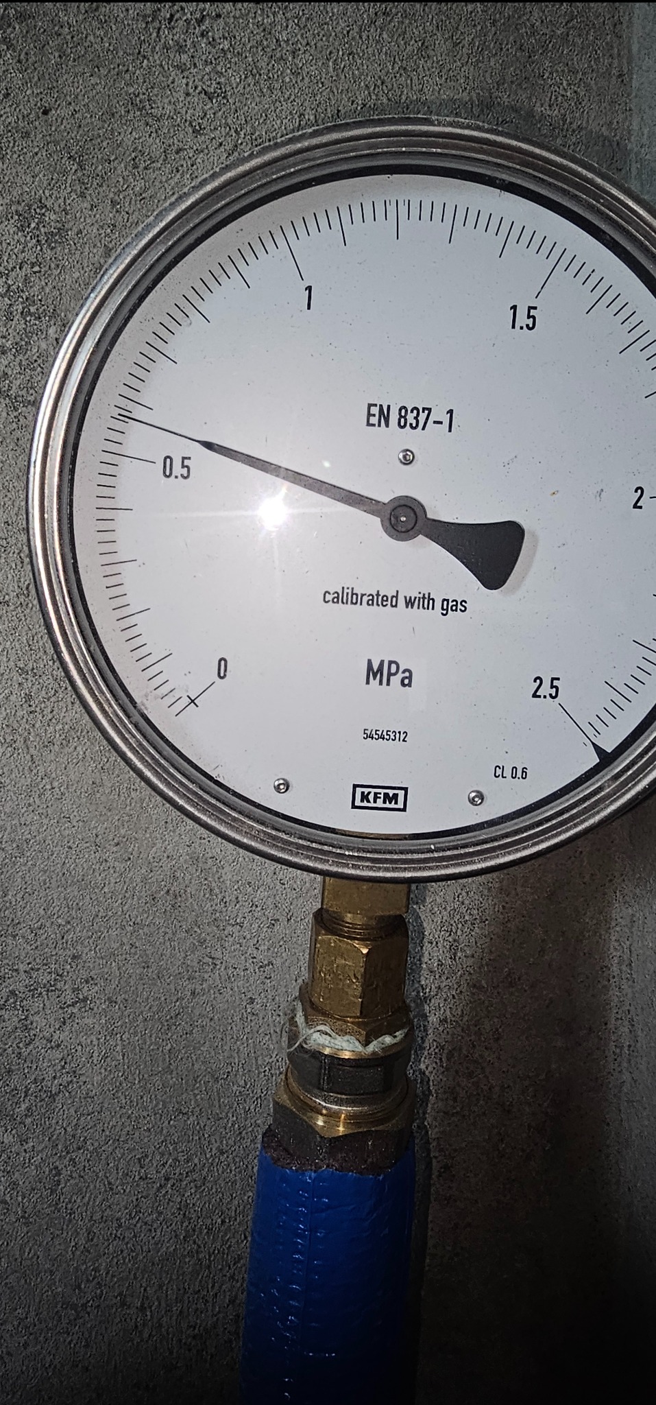 Manometr KFM wskazujący ciśnienie gazu, skala w MPa, podłączony do instalacji z niebieskim przewodem, widoczne ślady uszczelniania złączki.