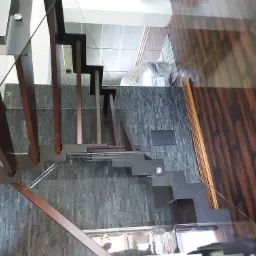 Nowoczesne schody z drewnianymi stopniami i szklaną balustradą, widok z góry, z elementami wykończenia ściany z kamienia łupkowego i drewnianej podłogi.