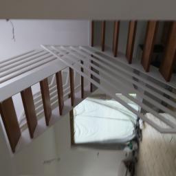 Usługi Stolarskie Marcin Biesiadecki - Widok z góry na białe schody z drewnianymi elementami w trakcie montażu, okno zabezpieczone folią malarską, niedokładne wykończenie.