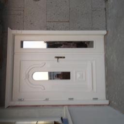 Usługi Stolarskie Marcin Biesiadecki - Białe drzwi wejściowe z przeszkleniami, widoczne elementy montażowe i surowy stan wykończenia ściany.