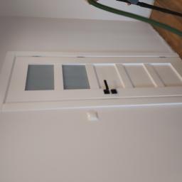 Usługi Stolarskie Marcin Biesiadecki - Białe, przeszklone drzwi wewnętrzne z czarną klamką, widoczne z boku, z zielonym wężem od odkurzacza w tle.