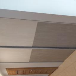 Usługi Stolarskie Marcin Biesiadecki - Fragment sufitu podwieszanego z kwadratowymi panelami w odcieniach beżu i szarości, widoczne także drewniane elementy zabudowy i oświetlenie liniowe.