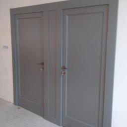 Usługi Stolarskie Marcin Biesiadecki - Dwa szare, zamknięte drzwi wewnętrzne z prostymi panelami, zamontowane w ścianie, widoczne klamki i klucze, podłoga wyłożona płytkami i panelami.