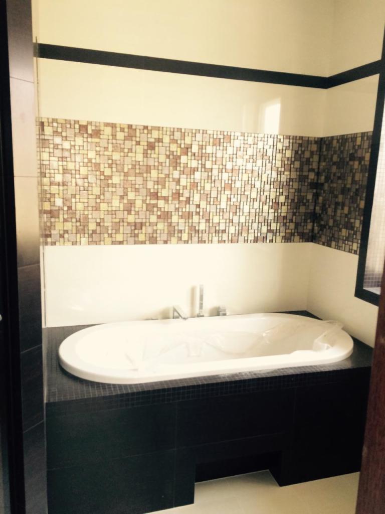 Nowoczesna łazienka z białą wanną obudowaną czarnymi płytkami mozaikowymi, ściana wyłożona mozaiką w odcieniach beżu i brązu, zabezpieczona folią ochronną.