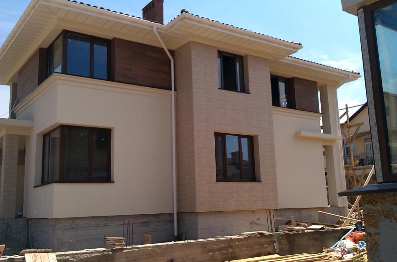 Dwukondygnacyjny dom murowany z elementami dekoracyjnymi elewacji w odcieniach beżu i brązu, z widocznymi fundamentami i elementami rusztowania.