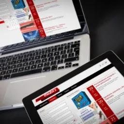 Laptop i tablet wyświetlające stronę internetową z kalendarzem wydarzeń i ofertą imprez, widok z góry na czarnym tle.