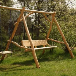 Drewniana huśtawka ogrodowa z siedziskiem i dodatkową platformą, wykonana z naturalnych pni i gałęzi, zawieszona na sznurach, umieszczona na trawniku w ogrodzie z kwitnącymi krzewami w tle.