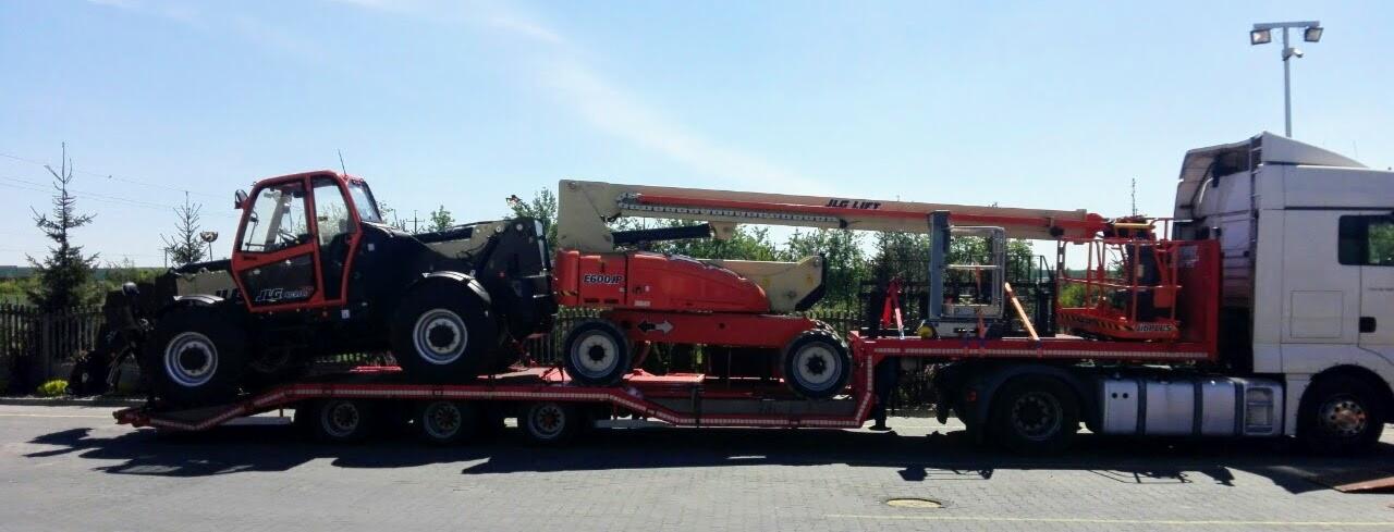 Dwie pomarańczowe platformy robocze JLG Lift przewożone na niskopodwoziowej naczepie ciągniętej przez biały ciągnik siodłowy w słoneczny dzień.