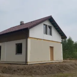 Budowa domu w Dobrzyniu nad Wisłą w trakcie montażu elewacji, widoczna konstrukcja i częściowo otynkowane ściany, na działce stoi niebieski samochód dostawczy.