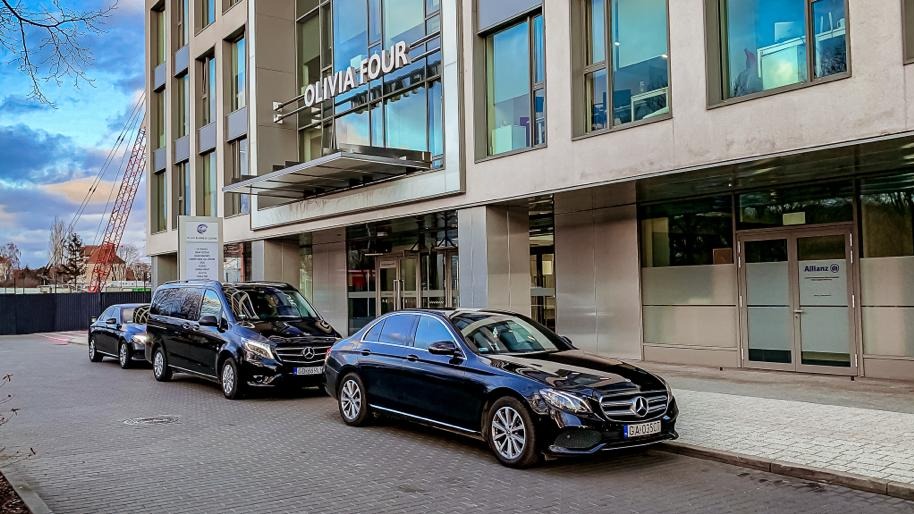 Flota czarnych samochodów Mercedes-Benz (sedan i van) zaparkowana przed nowoczesnym biurowcem Olivia Four z logo Allianz.