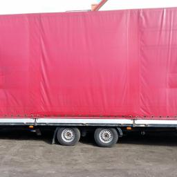 mariusz kruczyk - Czerwona plandeka naczepy ciężarowej z widocznymi mocowaniami i dwoma osiami kół, stojąca na ziemi