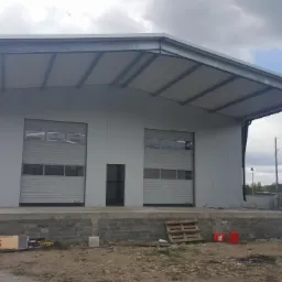 Nowoczesny magazyn z dwiema bramami rolowanymi, częściowo zadaszony, z rampą załadunkową i paletą leżącą na ziemi.