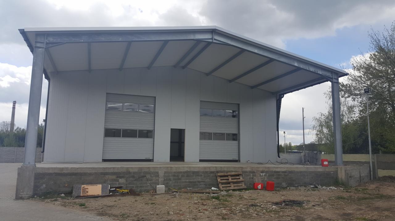 Nowoczesny magazyn z dwiema bramami rolowanymi, częściowo zadaszony, z rampą załadunkową i paletą leżącą na ziemi.