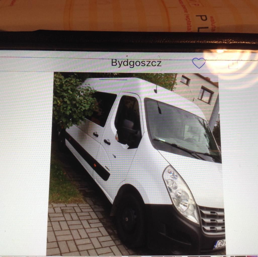 Biały bus Renault Master z czarnymi felgami i przyciemnionymi szybami, zaparkowany na brukowanym podjeździe przed zielonymi krzewami i domem w Bydgoszczy.