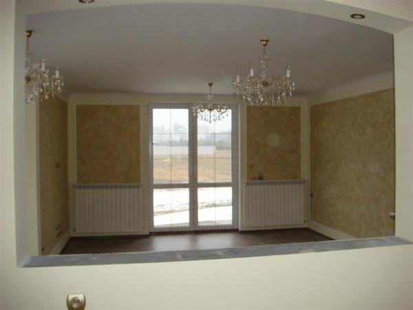 Salon po odświeżeniu z dekoracyjnymi ścianami w odcieniach beżu, kryształowe żyrandole i duże okno balkonowe z widokiem na zewnątrz.